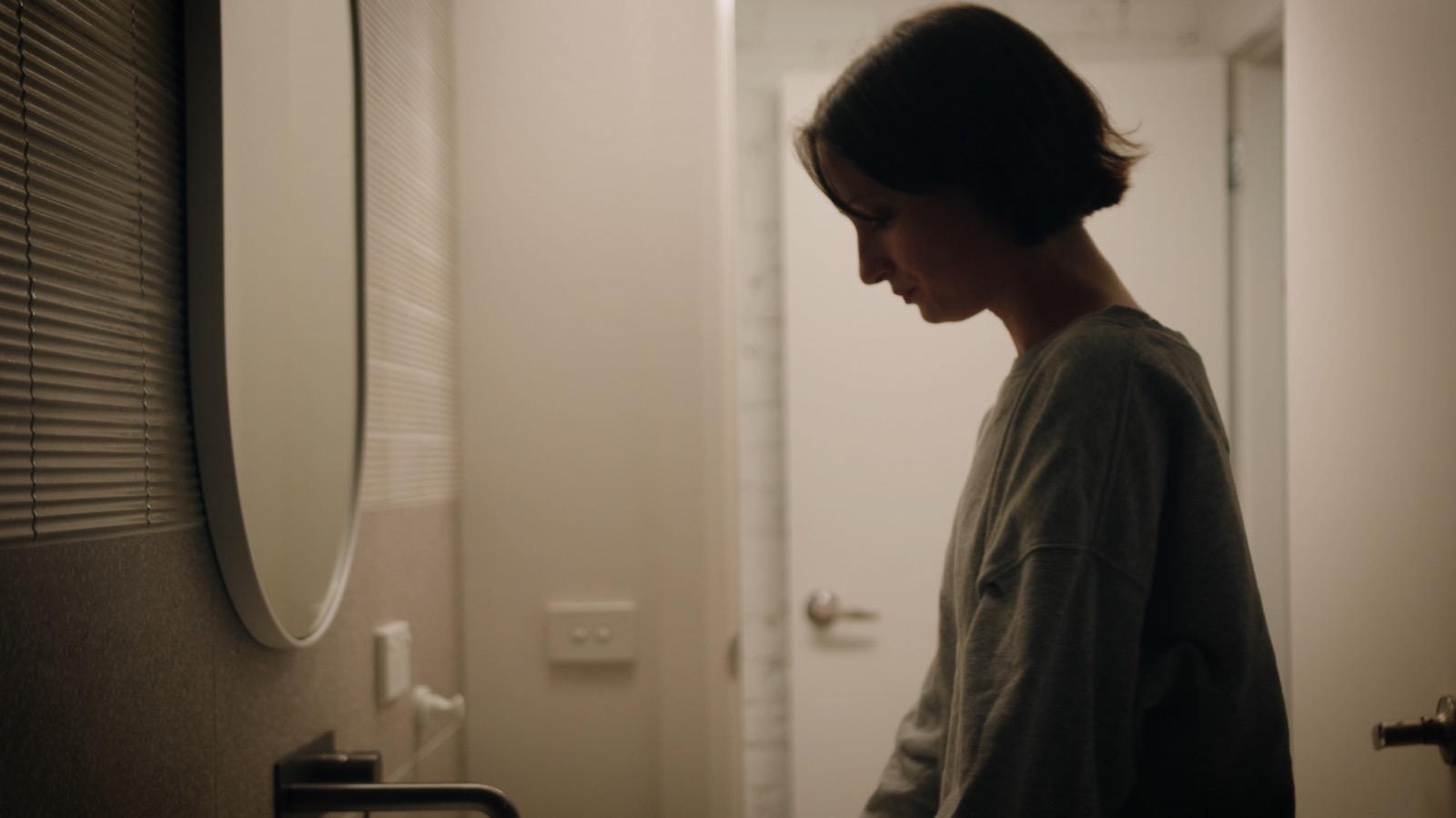 A woman standing in a doorway, looking down.