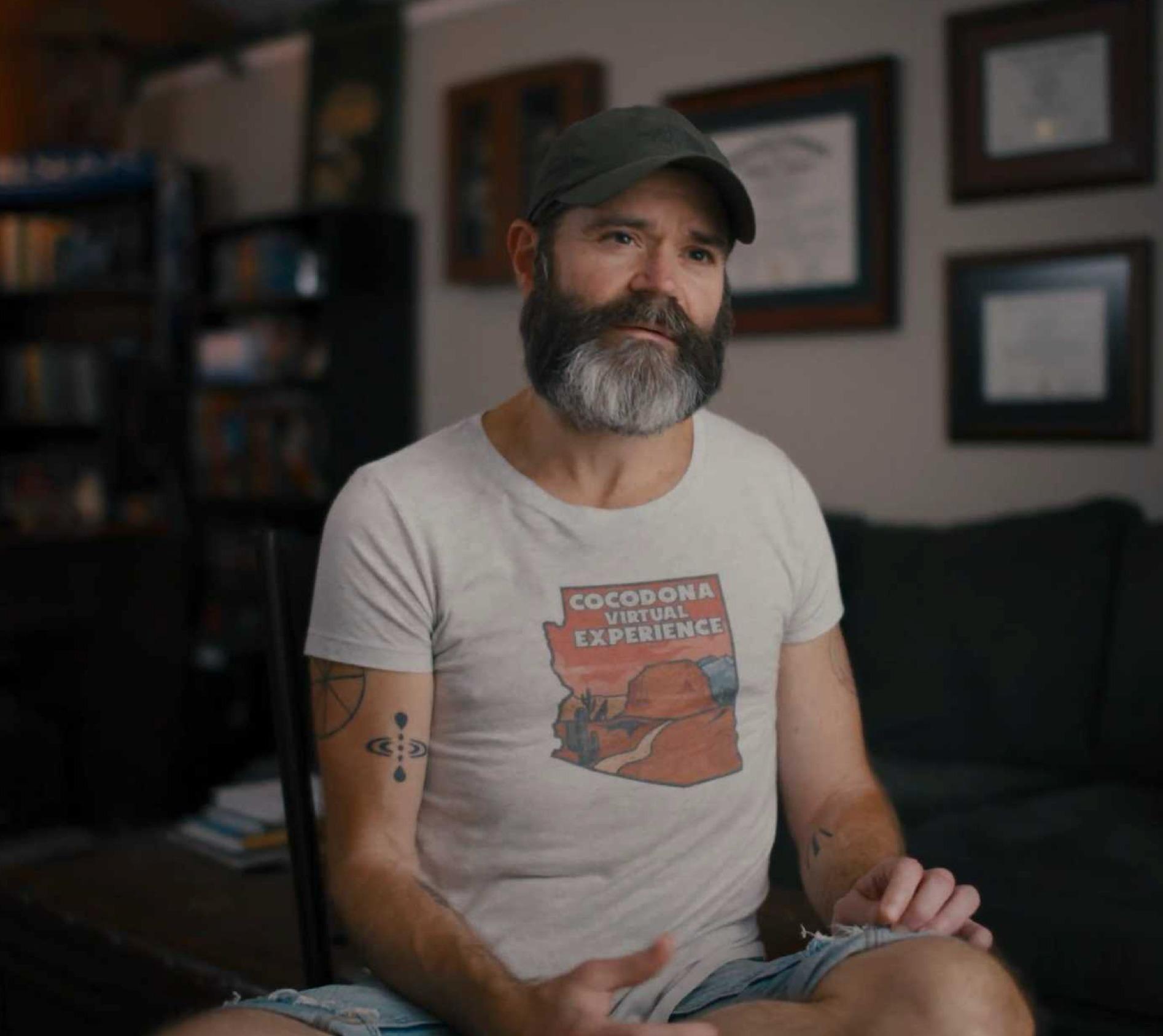 A man sitting cross-legged, talking to camera.